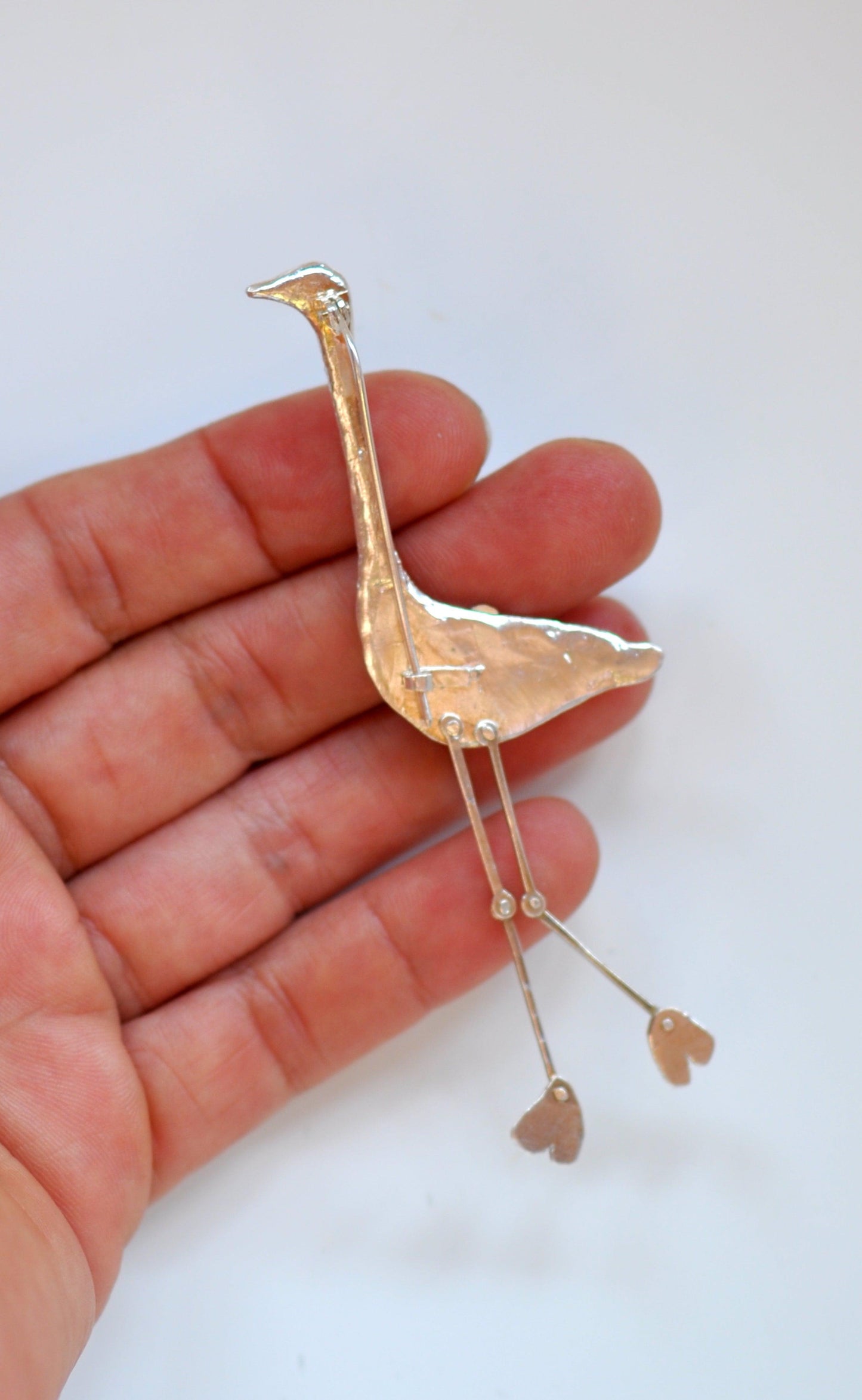 a hand holding a tiny gold bird brooch