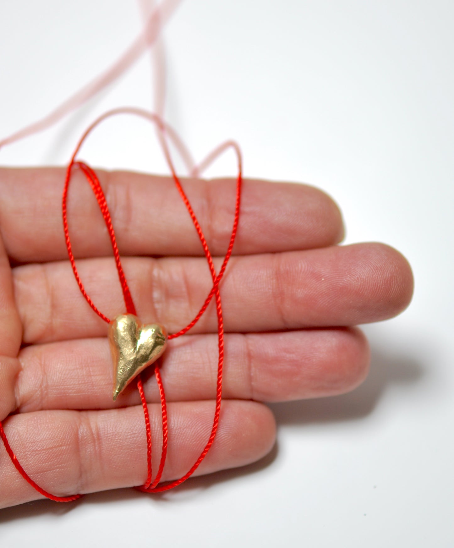 a hand holding a red string with a gold heart on it