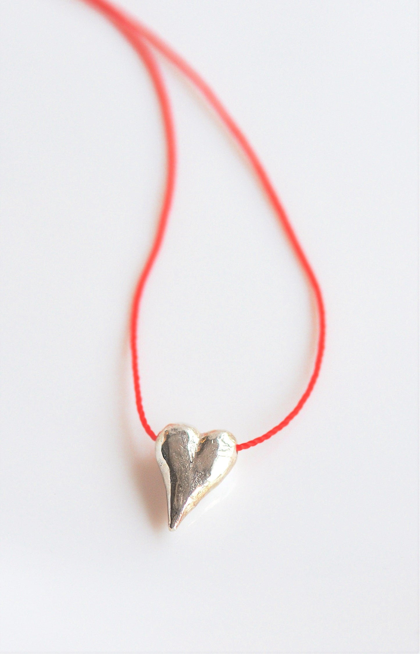 a silver heart pendant on a red string