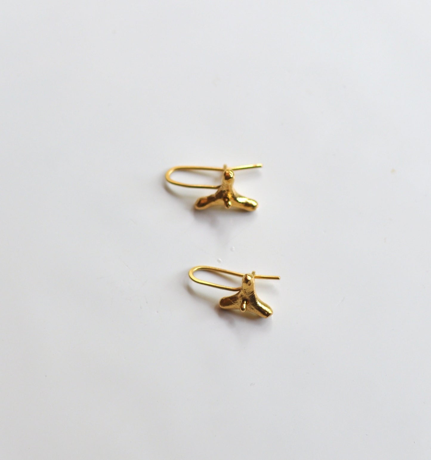 a pair of gold earrings sitting on top of a white surface