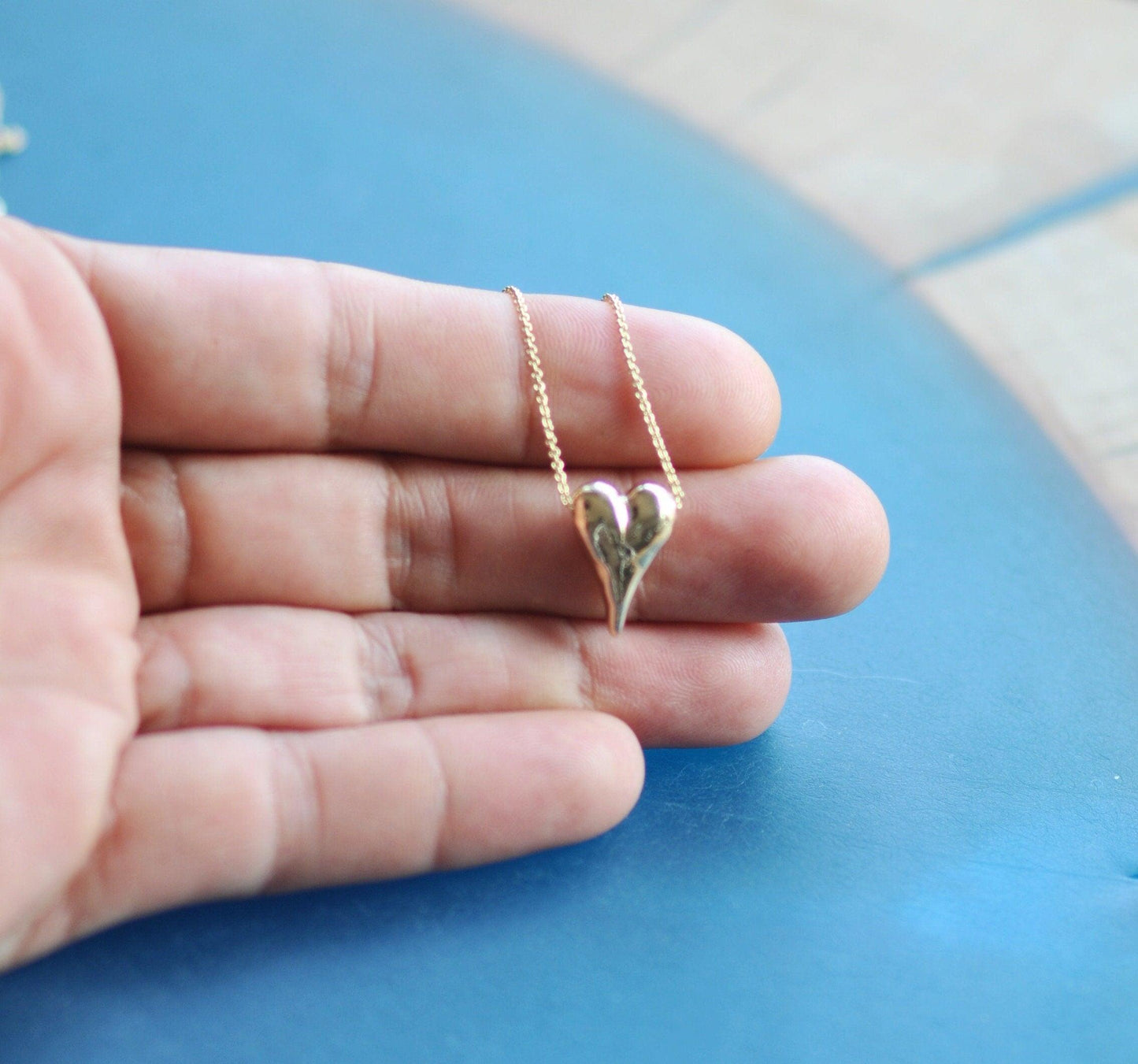 a hand holding a tiny gold heart necklace