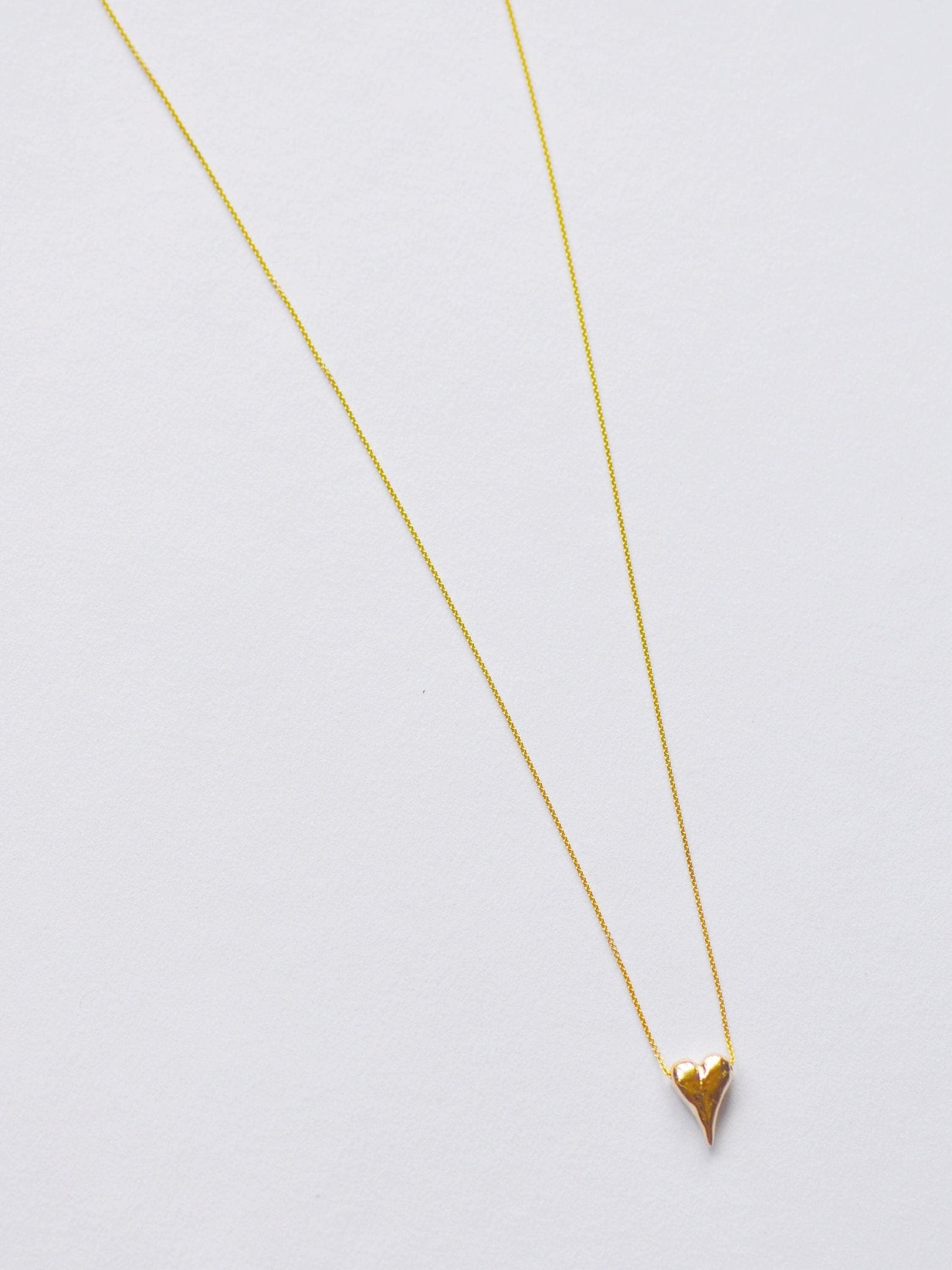 a gold necklace with a heart on a white background