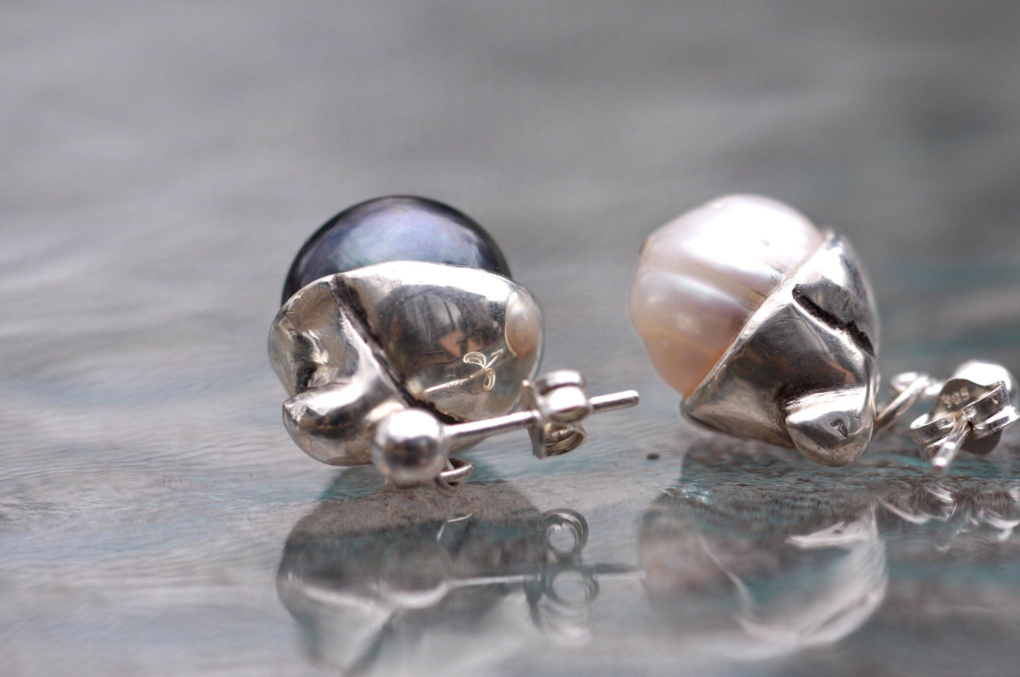 a pair of silver and pearl earrings on a reflective surface