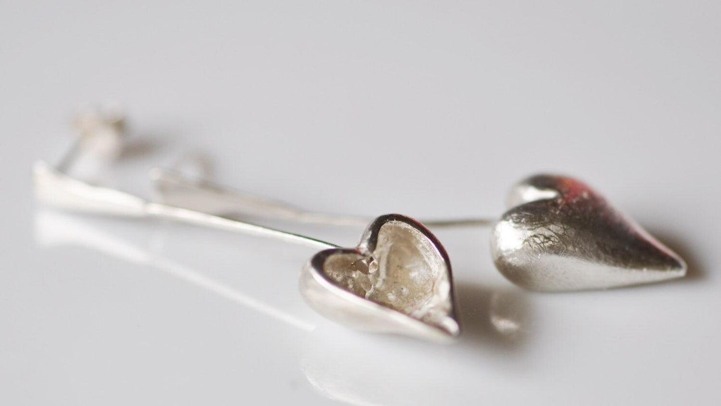 a pair of silver heart earrings on a white surface