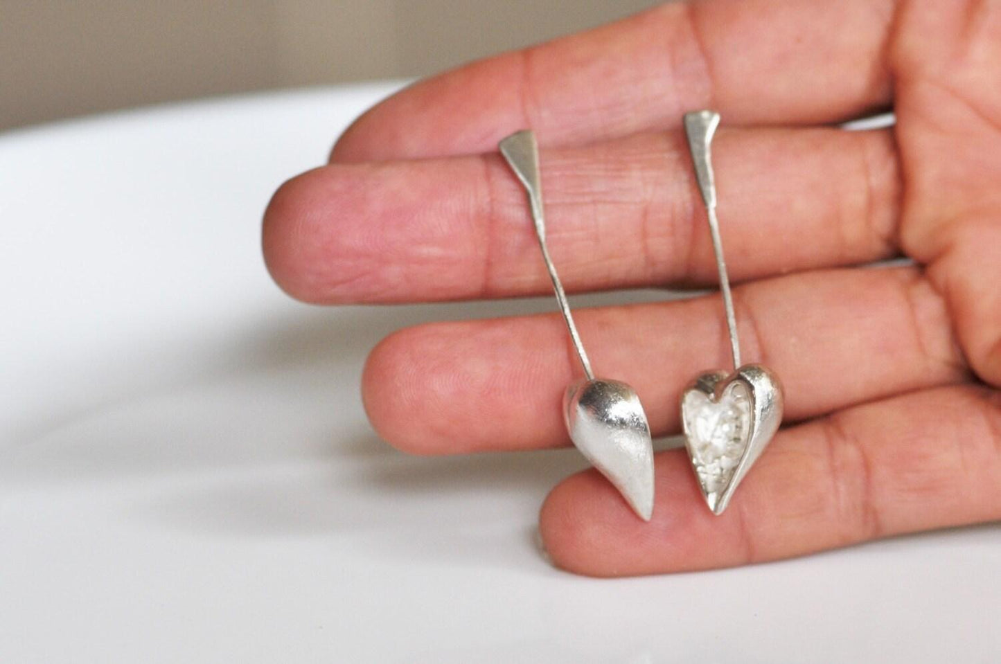 a hand holding a pair of silver heart shaped earrings