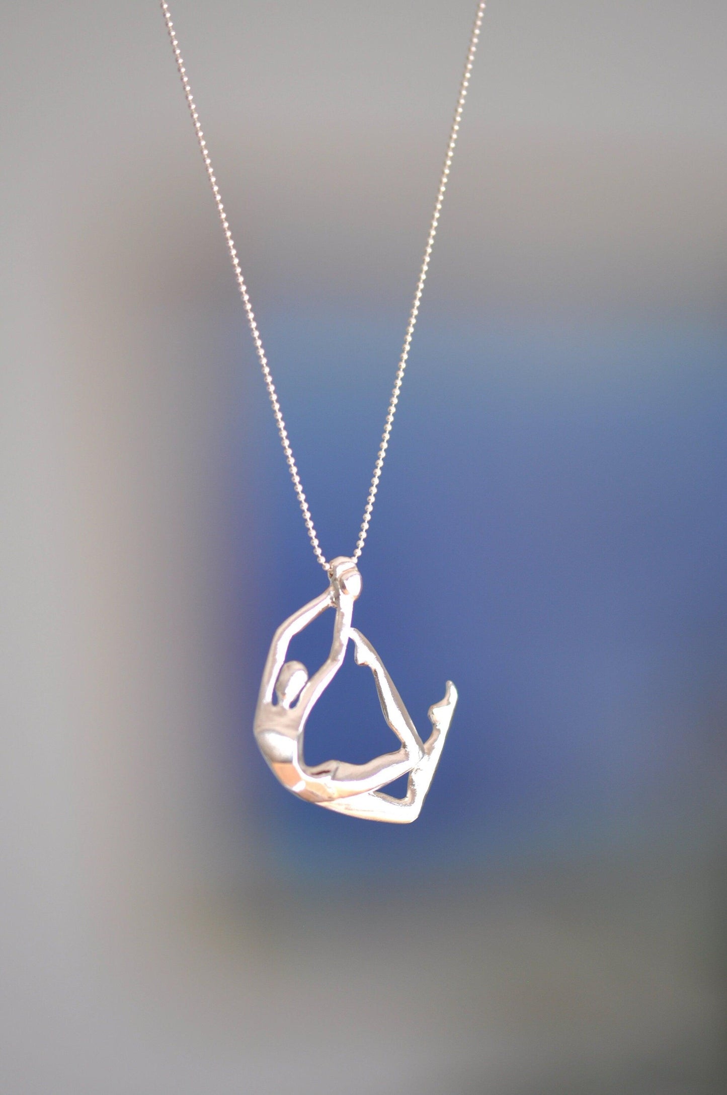 a silver necklace with a person doing yoga