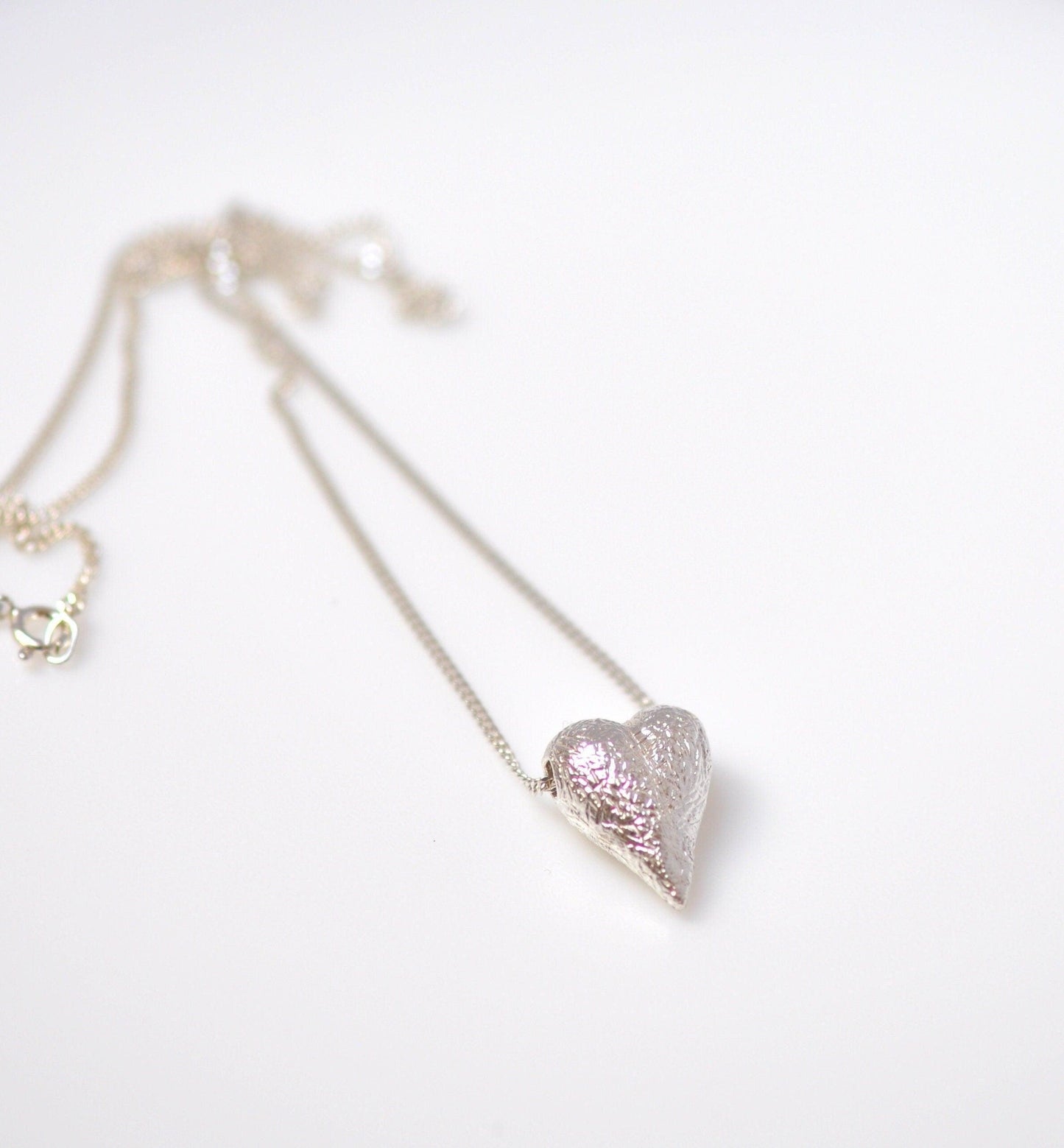 a heart shaped pendant on a chain on a white surface