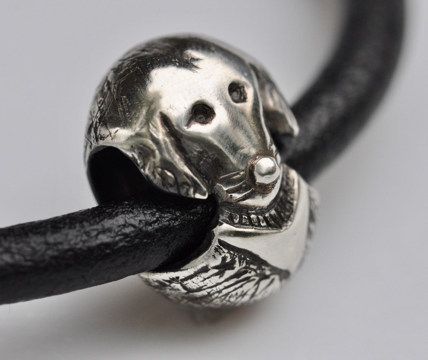 a close up of a silver dog head on a black leather cord