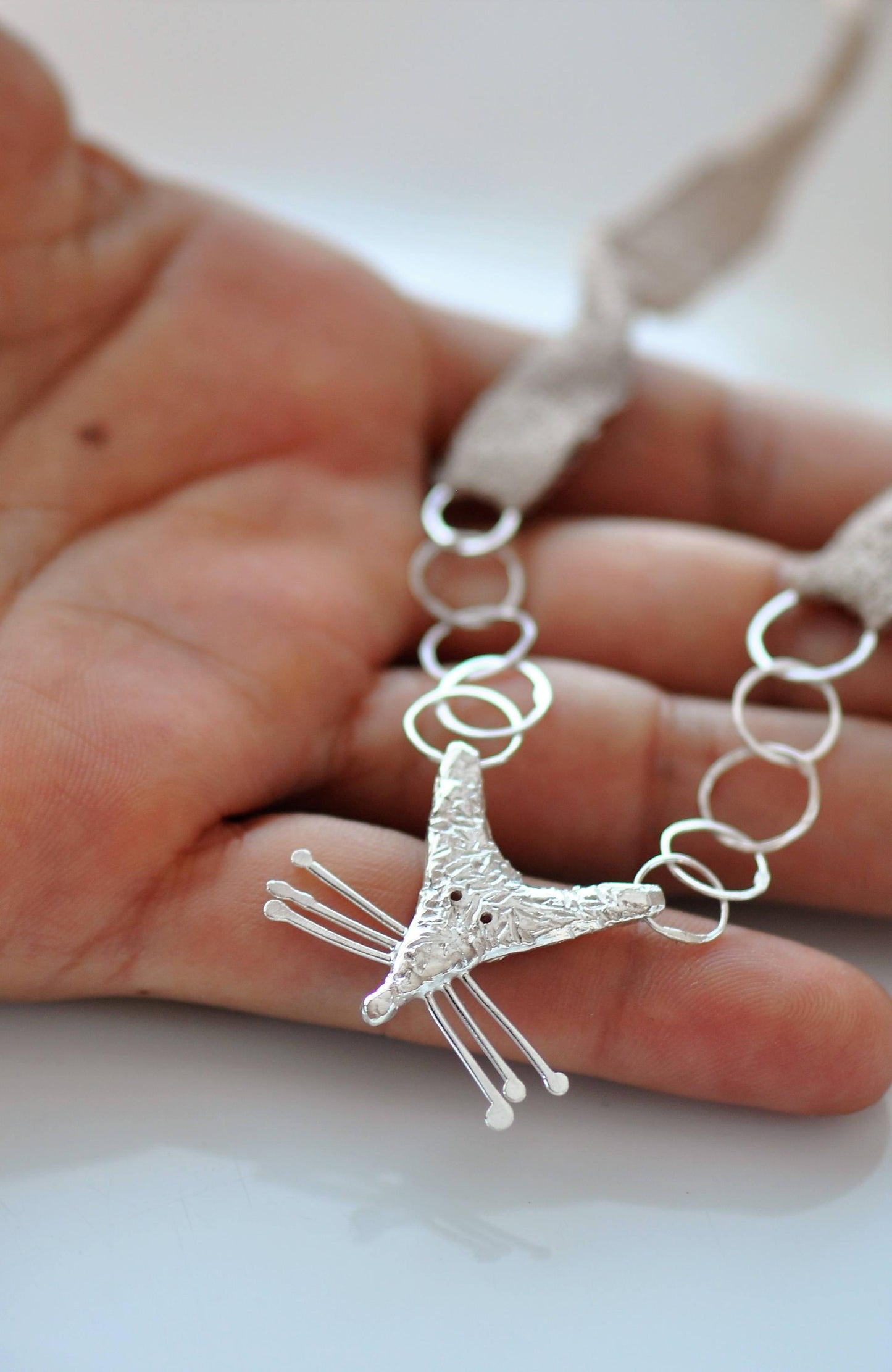 a hand holding a silver necklace with a giraffe on it