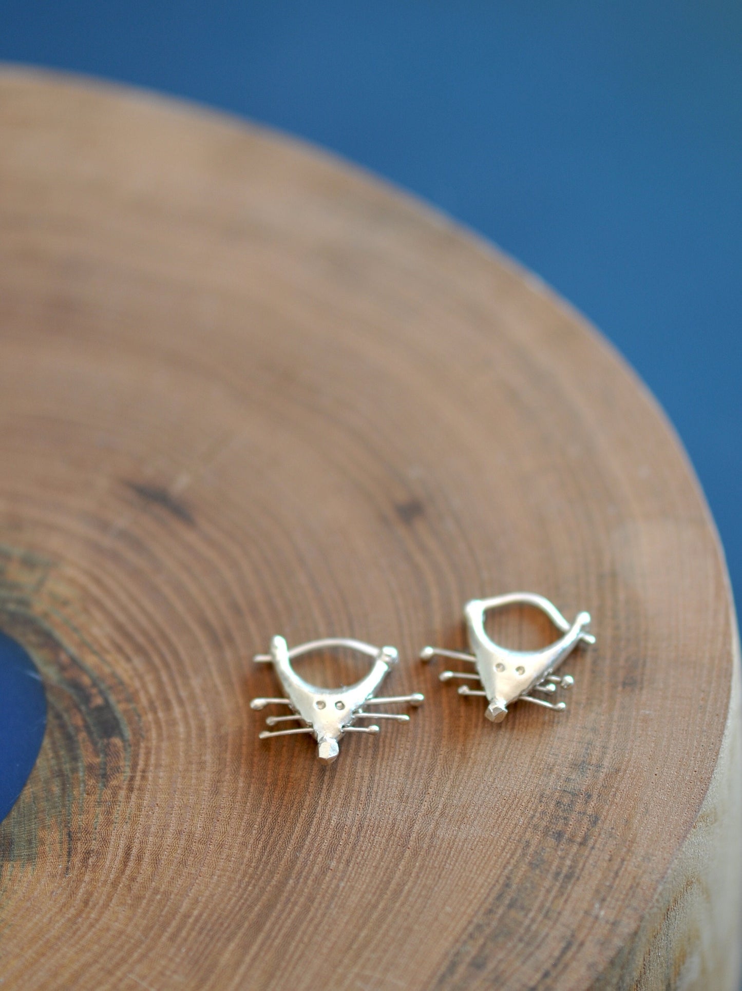 a pair of cat earrings sitting on top of a wooden table