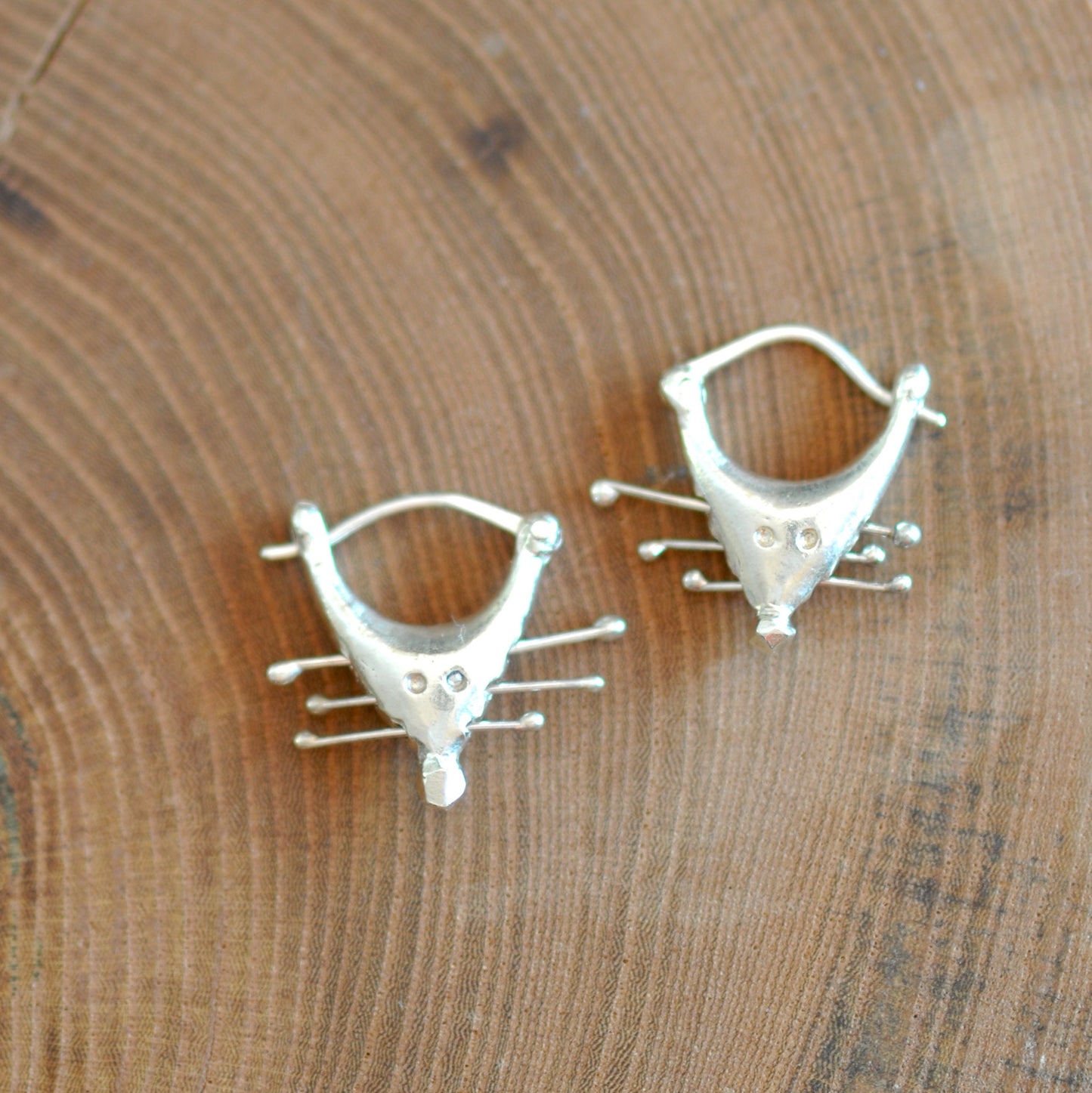 a pair of silver earrings sitting on top of a wooden table