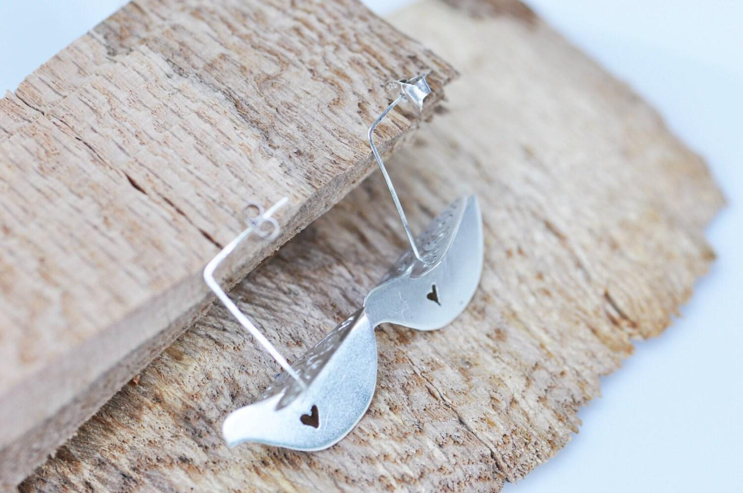 a pair of silver earrings sitting on top of a piece of wood