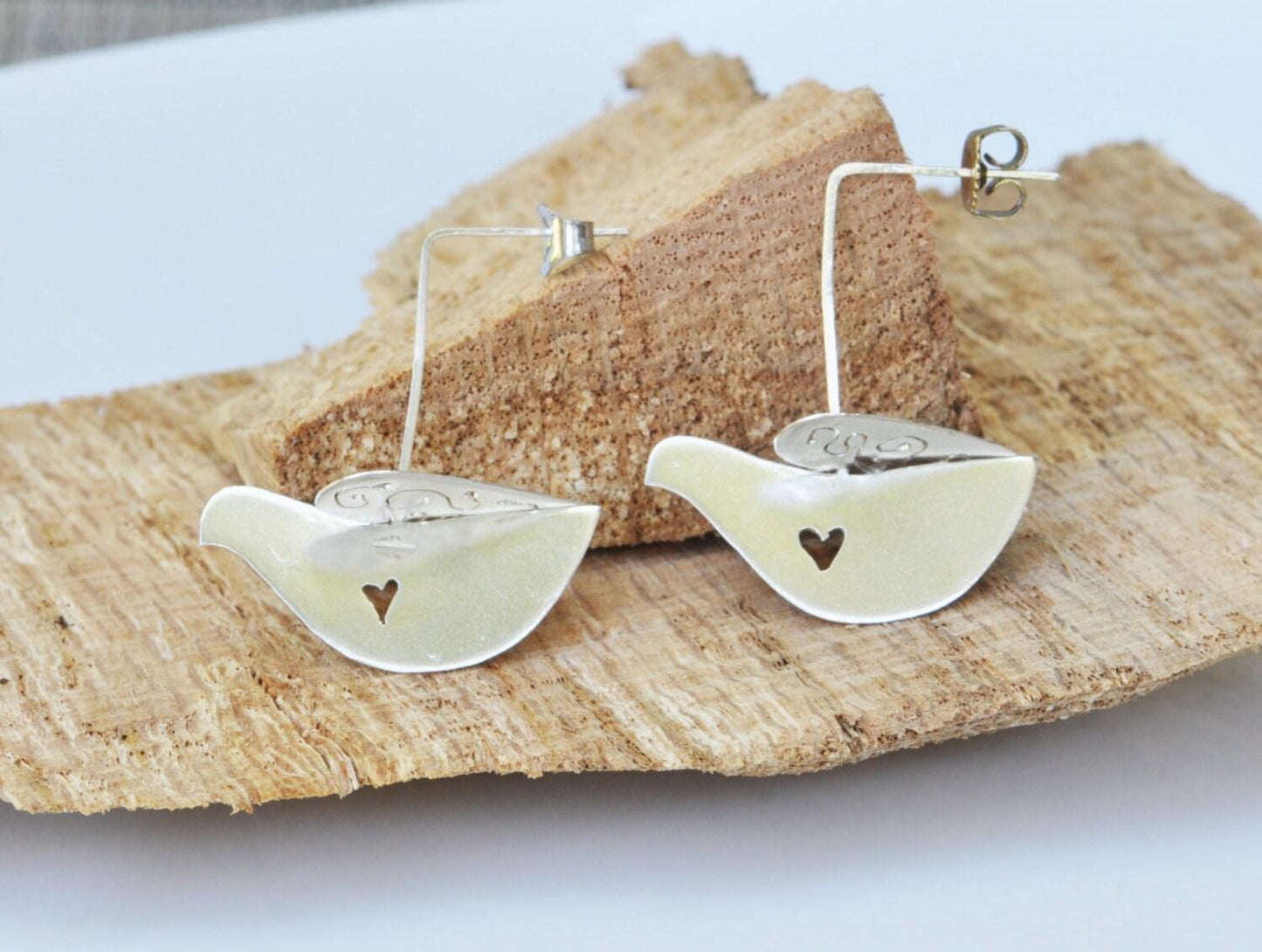 a pair of white bird shaped earrings on a piece of wood