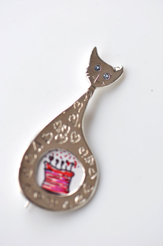 a silver cat brooch with a cake on it