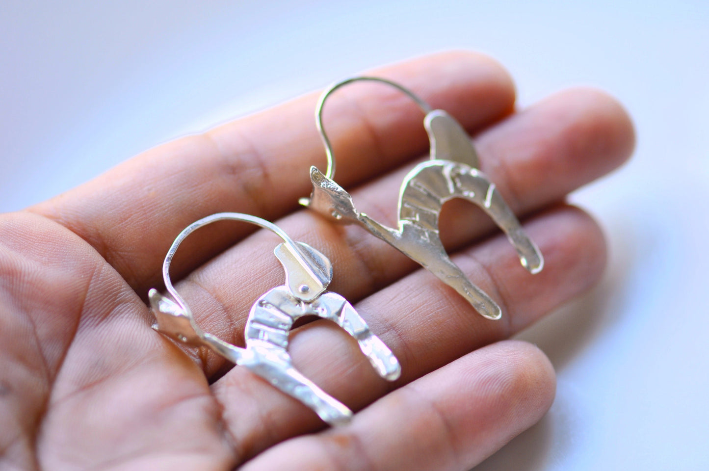 a pair of silver earrings sitting on top of a person's hand