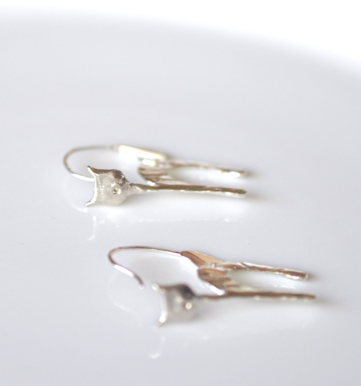 a pair of silver earrings sitting on top of a white table