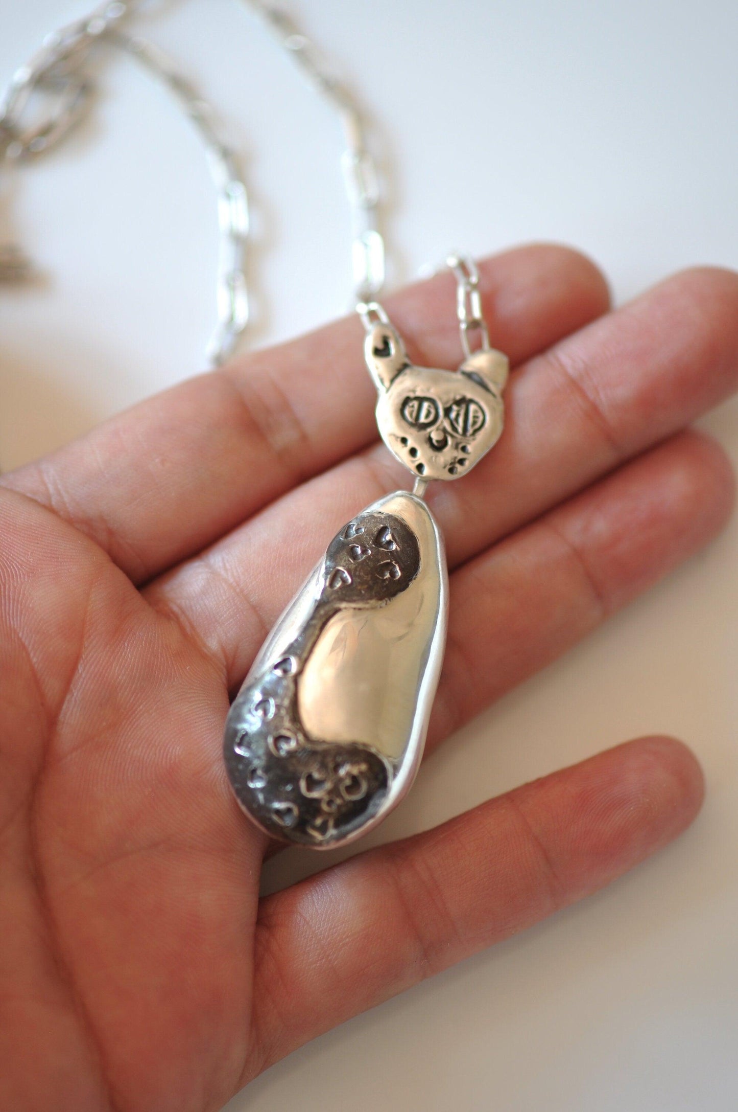 a person holding a silver necklace with a heart