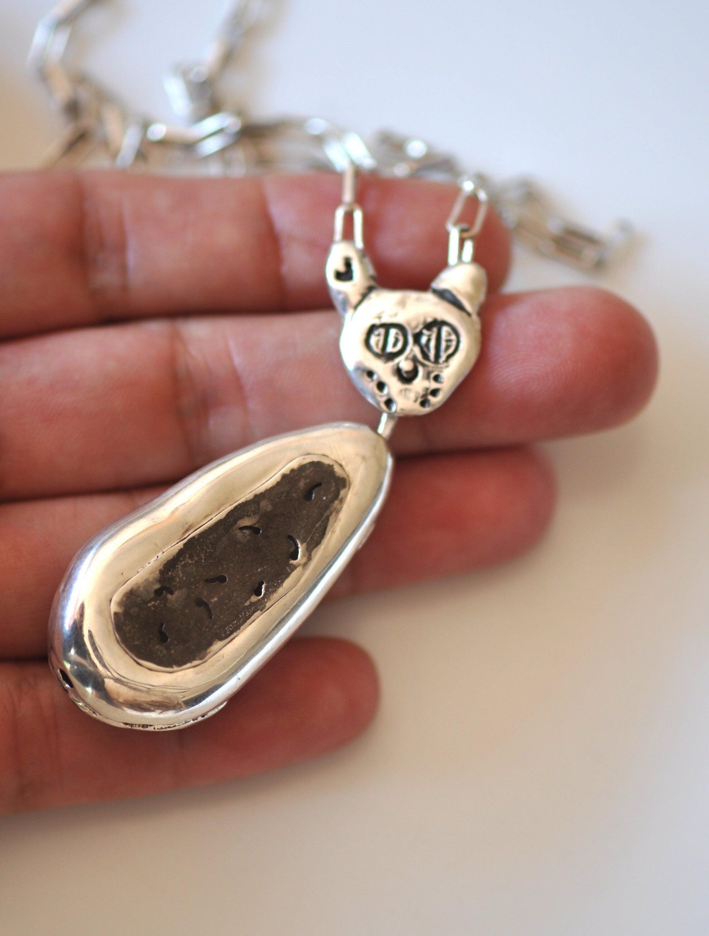 a hand holding a silver pendant with a dog paw on it